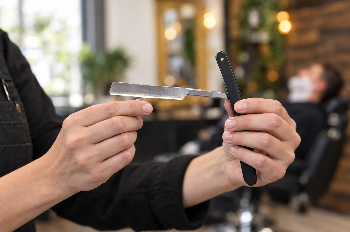 Barbière tenant un rasoir coupe-chou ouvert, prête à raser un client dans l'espace barbier du Salon Mickael Roman